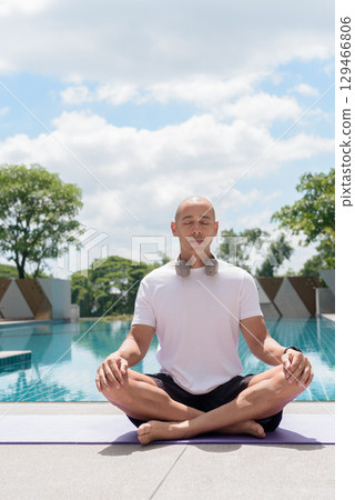 Man practicing yoga meditation by pool, wellness, mindfulness and healthy outdoor lifestyle concept 129466806