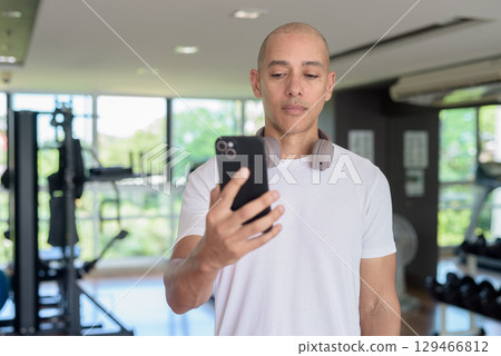 Bald Hispanic man using phone in gym, workout lifestyle, digital fitness and modern training routine Bald Hispanic man using phone in gym, workout lifestyle, digital fitness and modern training routine 129466812