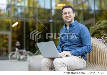 Businessman working with a laptop in an urban outdoor environment, conveying technology and modern work. 129467172