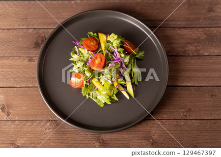 Plate with fresh salad: colorful mix of lettuce, tomatoes, cucumbers, and carrots drizzled with vinaigrette Plate with fresh salad: colorful mix of lettuce, tomatoes, cucumbers, and carrots drizzled with vinaigrette 129467397