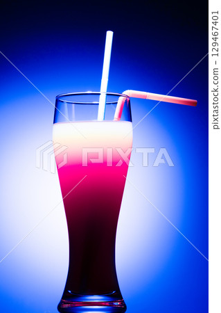 A layered cocktail in a tall glass, featuring distinct white, pink, and dark red purple layers, illuminated against a  129467401