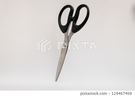 A pair of silver-bladed scissors with black handles stands upright on a plain white background A pair of silver-bladed scissors with black handles stands upright on a plain white background 129467409
