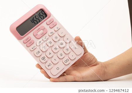 A person's hand holds a small, portable, pink calculator with a digital display showing 455459 against a clean white background 129467412