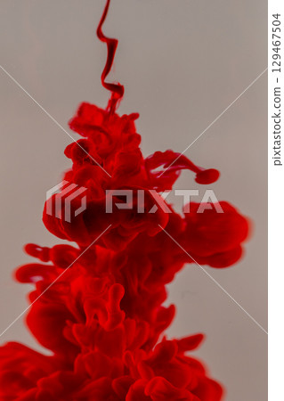 Red ink dispersing in water, creating abstract shapes and patterns 129467504