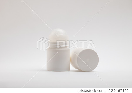 A white, unlabeled roll-on deodorant bottle stands upright next to its detached cap, which lies horizontally on a clean, 129467555