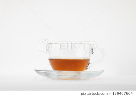 A clear glass teacup filled with amber-colored tea, possibly black or rooibos, resting on a matching clear glass saucer A clear glass teacup filled with amber-colored tea, possibly black or rooibos, resting on a matching clear glass saucer 129467664