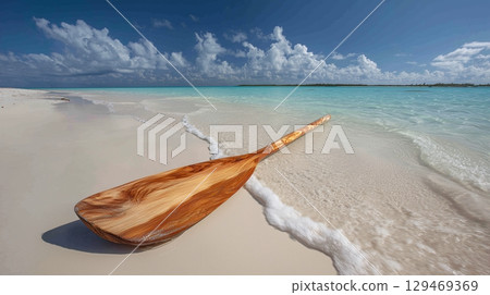 Beautiful wooden paddle resting on soft sandy beach near turquoise water under a blue sky with fluffy clouds 129469369