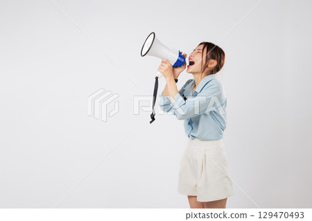 Young woman holds a megaphone, ready to shout important news and an announcement. Her mouth is set for speaking, actively screaming with her impactful megaphone. isolated studio white background 129470493