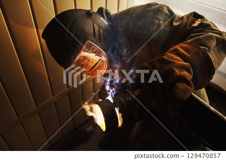 Worker in safety mask welds metal at industrial enterprises. Worker in safety mask welds metal at industrial enterprises. 129470857