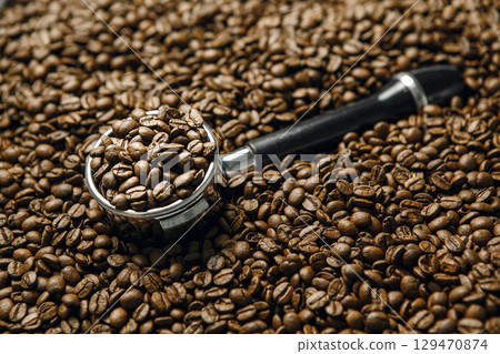 Espresso Portafilter Filled With Coffee Beans Lies on Roasted Beans, Close-up. Concept of Espresso Serving. Espresso Portafilter Filled With Coffee Beans Lies on Roasted Beans, Close-up. Concept of Espresso Serving. 129470874