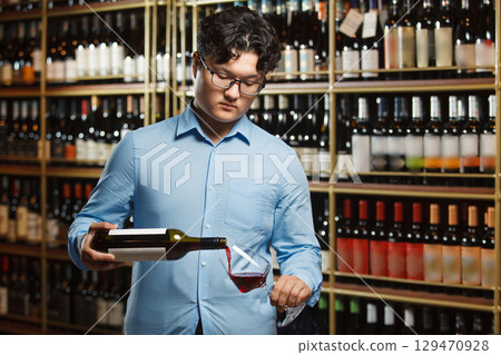 Asian Professional Sommelier Carefully Pours Red Wine in Glass at an Elegant Wine Shop 129470928