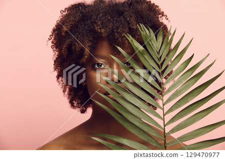 Sexy black girl watching intently from behind palm leaves. 129470977
