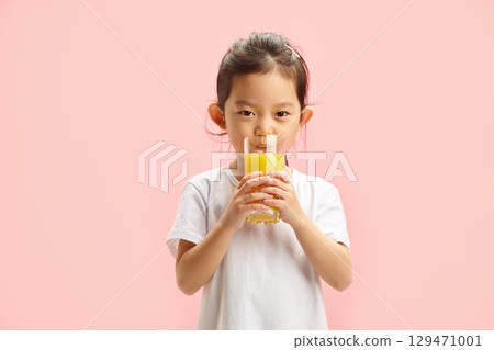 Beautiful Cute Little Girl Drinking Orange Juice From Round Glass Standing Over Pink Isolated 129471001