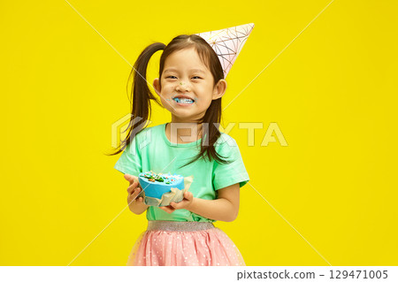 Joyful Child Girl Dressed in Party Clothes Enjoying Birthday Cake and Cheerful Smiling Over Yellow Isolated 129471005