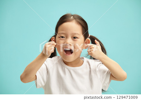 Female japanese child with mouthly wide open clean myself her teeth with a dental floss, close up isolated portrait. Five years old asian ethnicity girl using oral hygiene staff. 129471009