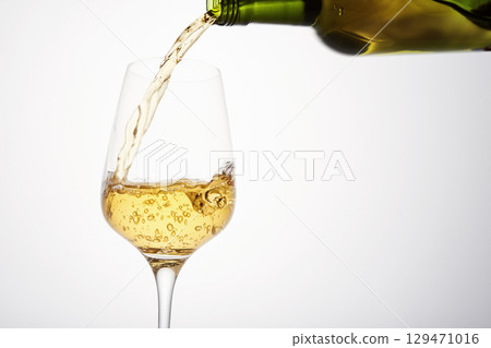 White wine pouring from green bottle, close up. 129471016