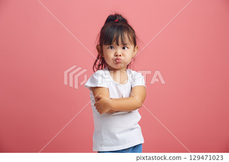 Offended little asian girl with insulted expression, stick out lips in discontent, has negative mood,crossed hands in front of her poses over pink 129471023