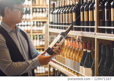 Asian Sommelier Selecting Fine Wine Bottle From Wooden Cellar Shelf Asian Sommelier Selecting Fine Wine Bottle From Wooden Cellar Shelf 129471167