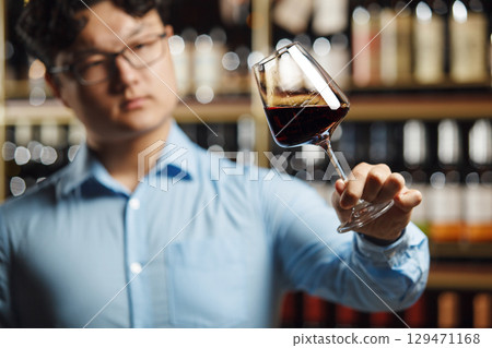 Asian Sommelier Carefully Evaluating Red Wine In Well-Stocked Cellar Asian Sommelier Carefully Evaluating Red Wine In Well-Stocked Cellar 129471168