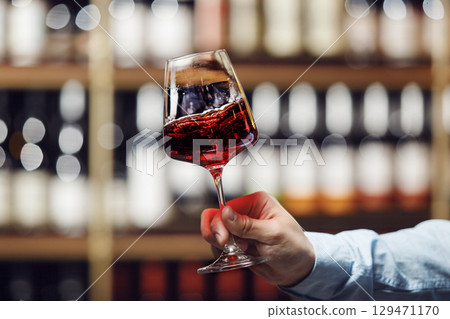 Close-Up of Sommelier Swirling Glass of Red Wine in Well-Stocked Wine Cellar with a Free Copy Space Close-Up of Sommelier Swirling Glass of Red Wine in Well-Stocked Wine Cellar with a Free Copy Space 129471170