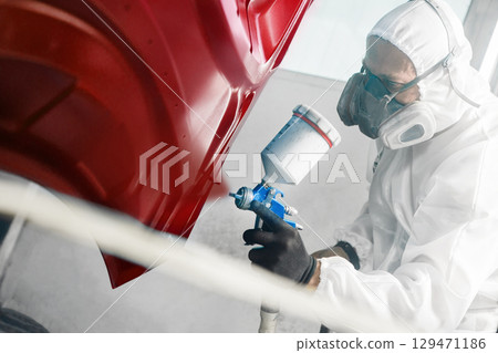 Car painter sprays red color paint to part of vehicle using spray gun in workshop garage. Complex repair and restoration automobile with exact select of color after accident. Car painter sprays red color paint to part of vehicle using spray gun in workshop garage. Complex repair and restoration automobile with exact select of color after accident. 129471186
