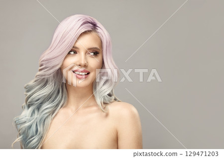 Cheerful woman with long curly pink and blue color hair looks aside on beige background. Cheerful woman with long curly pink and blue color hair looks aside on beige background. 129471203