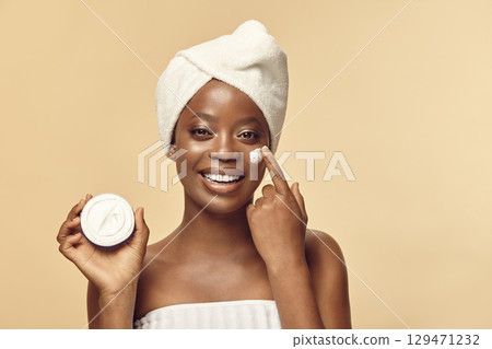 Positive brown skinned girl applying cream to her face. 129471232