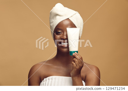 Playful black girl in towel holds tube mockup in front of her face. 129471234