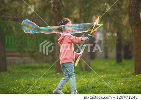 Happy Girl Blows Large Bubble in Park on Sunny Day 129471248