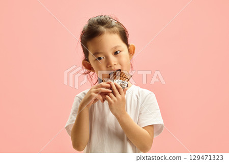 Cute and Happy Asian Child Enjoying Eat Chocolate Bar with a Pleasure Face on a Pink Isolated Cute and Happy Asian Child Enjoying Eat Chocolate Bar with a Pleasure Face on a Pink Isolated 129471323