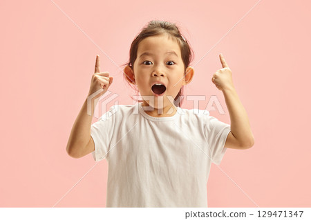 Sweet korean child girl looks amazed points at something up and looking to camera, isolated on a pink background. Cute little kid sees an amazing thing up, gestures indoor Sweet korean child girl looks amazed points at something up and looking to camera, isolated on a pink background. Cute little kid sees an amazing thing up, gestures indoor 129471347