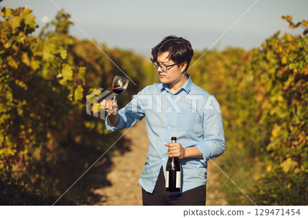 Asian Sommelier Tasting Red Wine in Sunlit Vineyard 129471454