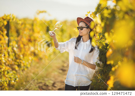 Female Sommelier Evaluating White Wine in the Midst of a Vineyard During Sunny Afternoon Female Sommelier Evaluating White Wine in the Midst of a Vineyard During Sunny Afternoon 129471472