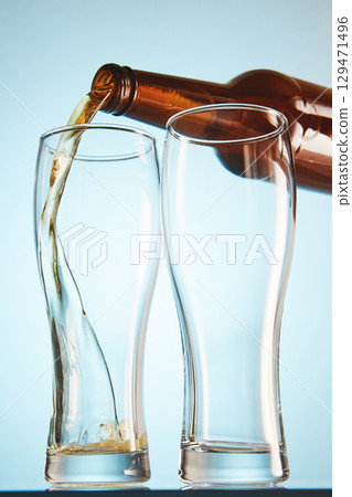 Lager, ale flows to empty tall glasses from bottle. 129471496