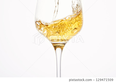 Stream of white wine flows into stem glass, swirls. 129471509