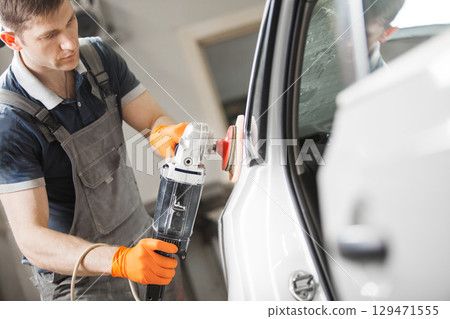 Man polishes white car in auto repair shop, close-up. Orbital polishing machine. Polished finishing. 129471555