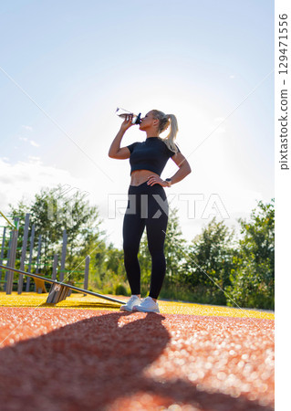 Female athlete resting and hydrating during outdoor functional fitness workout 129471556