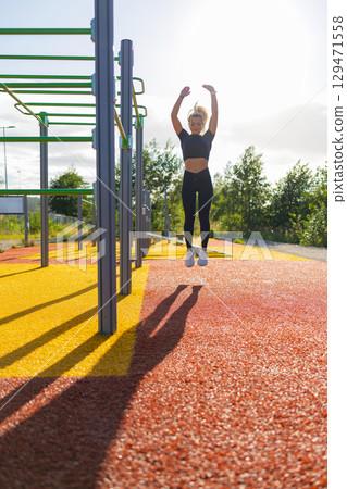 Woman Performing Jump Exercise at Outdoor Fitness Park on a Sunny Day 129471558