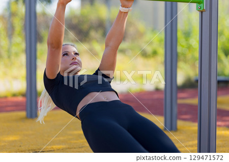 Woman performing pull-up exercise in outdoor fitness park with a focus on strength 129471572