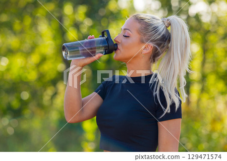 Woman outdoors drinking water from a bottle during a fitness activity 129471574