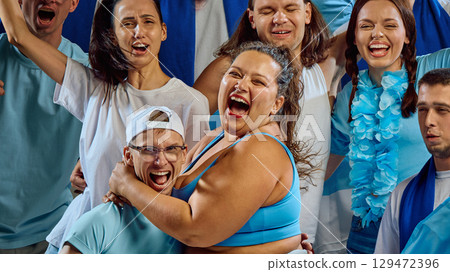 Plus size woman in blue sportswear hugging friend at fan zone event 129472396