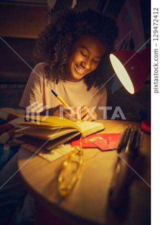 Teen girl smiling while writing in notebook under red lamp 129472412