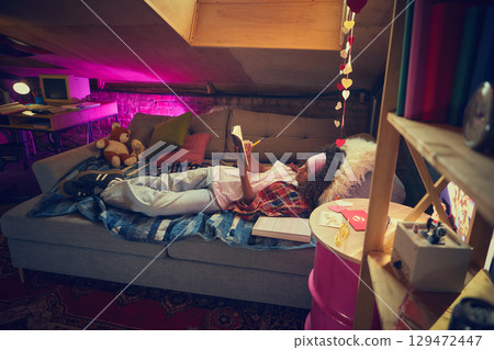 Teen girl relaxing with book in retro attic room Teen girl relaxing with book in retro attic room 129472447