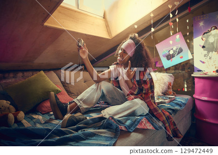 Teen girl making playful selfie in retro attic bedroom Teen girl making playful selfie in retro attic bedroom 129472449
