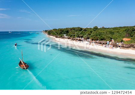Zanzibar beach scene with dhow boats and tourists enjoying the turquoise water Zanzibar beach scene with dhow boats and tourists enjoying the turquoise water 129472454