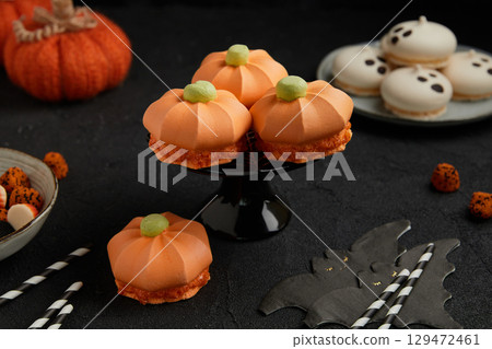 Four pumpkin shaped meringue desserts on a black stand with ghost cookies in the background Four pumpkin shaped meringue desserts on a black stand with ghost cookies in the background 129472461