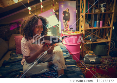 Teen girl enjoying retro magazine in colorful attic bedroom 129472572