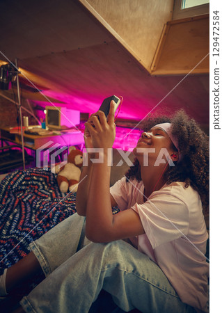 Teen girl smiling while listening to music in cozy retro attic room 129472584