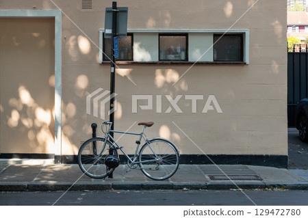 A bicycle leans against a street signpost on a sidewalk next to a light-colored building. 129472780