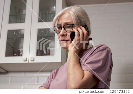 A Concerned Senior Woman on the Phone Portraying Emotion and Connectivity in a Modern Kitchen Environment A Concerned Senior Woman on the Phone Portraying Emotion and Connectivity in a Modern Kitchen Environment 129473332